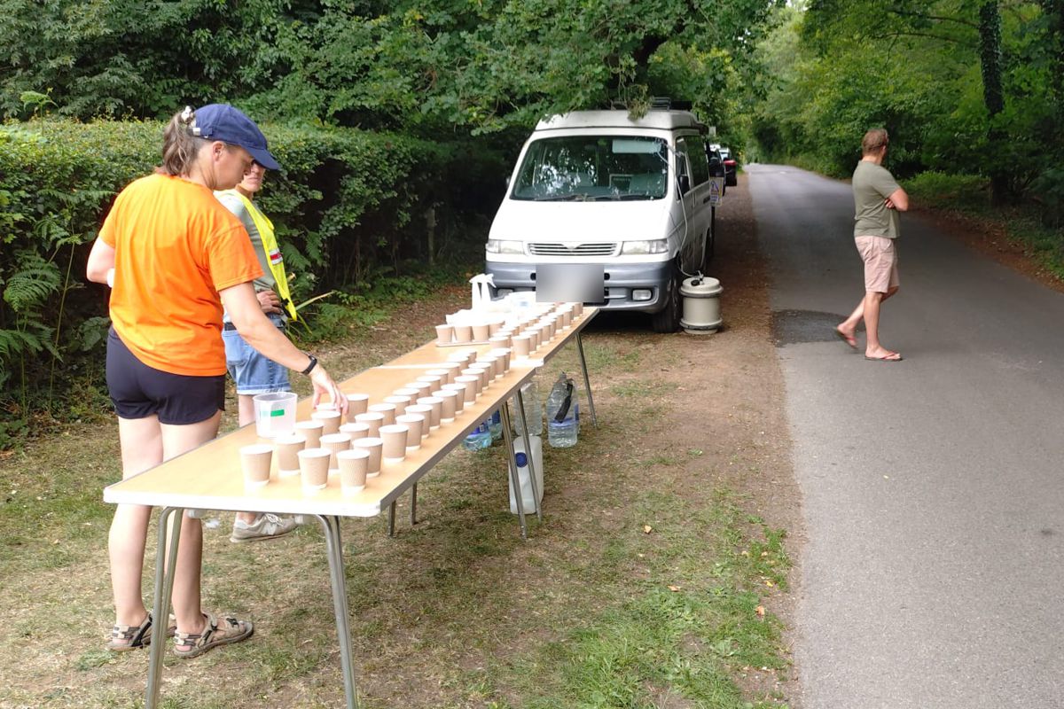 Volunteers setting out rows of cups at the water station on a tree-lined lane, 2025